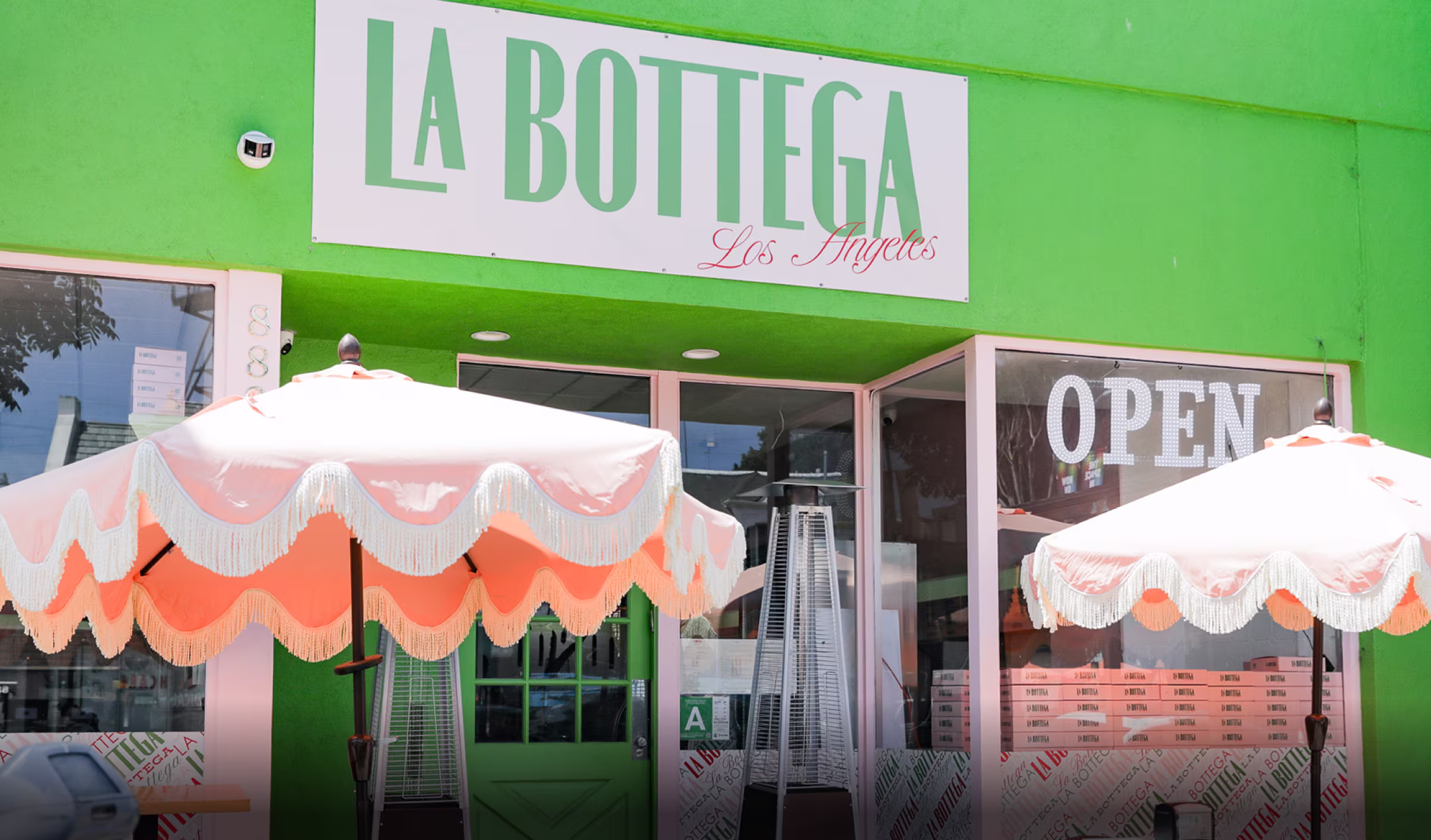 Vibrant Green Storefront With Pink Fringe Patio Umbrellas, Patio Heaters, Prominent Open Sign, And Customizable Exterior Signage Ideal For Outdoor Café Branding And Street-Level Retail Visibility