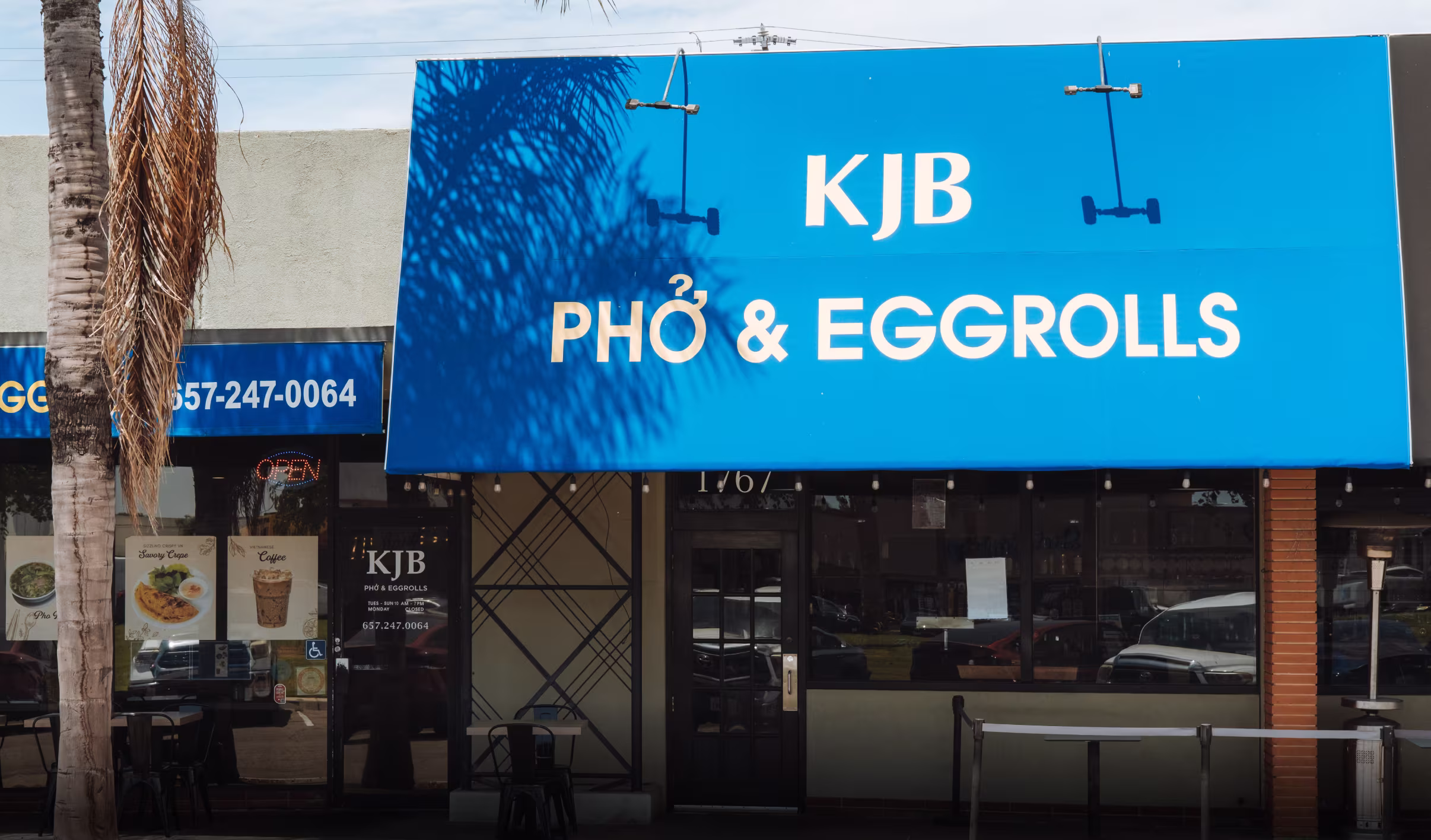 Blue Restaurant Awning Featuring Phở & Eggrolls Bold Text, Side Window Menus And Open Sign Promoting Dine‑In, Takeout, And Contact Number For Orders